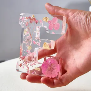 Primo piano di una lettera E in resina trasparente con fiori secchi rosa e foglia d'oro