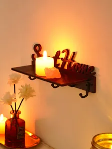 Detailopname van een houten wandplank met Sweet Home tekst en haken in warm kaarslicht.
