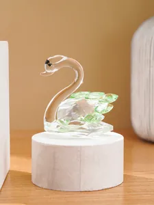 Detailed view of an elegant crystal swan figurine with green wings on a white wooden pedestal