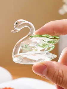 Close-up detail of a small green and clear crystal swan figurine held between fingers