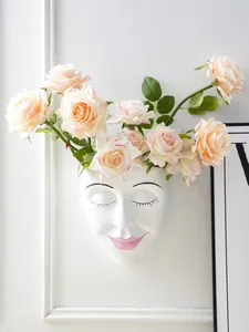 Close-up detail of a minimalist white resin human face flower pot with peach roses on a wall.