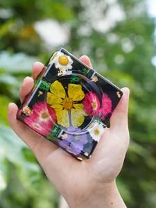Mano sosteniendo un cenicero de resina con flores secas coloridas y pan de oro