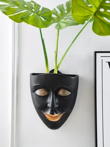 Detail of a minimalist black and gold face-shaped resin wall-mounted planter.