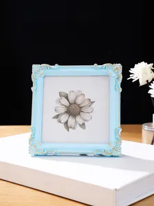Detailaufnahme eines blauen Relief-Fotorahmens mit Goldverzierung und Gänseblümchen