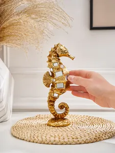 Hand holding a golden seahorse resin figurine with mirror details on a mat