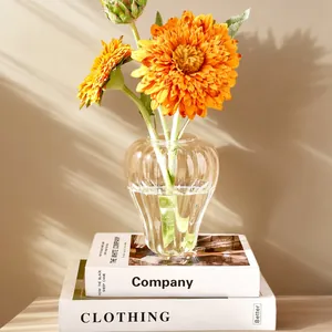 Detalle de un florero de vidrio transparente con costillas y forma de calabaza y gerberas