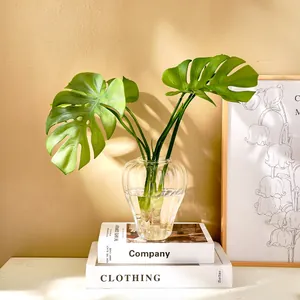Detalle elegante de un jarrón de vidrio con forma de calabaza y hojas de monstera en libros