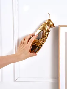 Vue détaillée d'une décoration murale miroir criquet en résine dorée avec main pour l'échelle