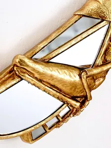 Détail d'une décoration murale en forme de criquet en résine dorée avec miroirs.