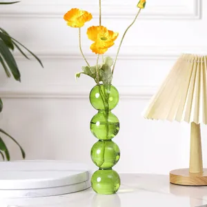 Moderne grüne Glasvase mit künstlichen orangefarbenen Mohnblumen auf einem Marmortisch