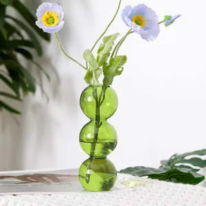 Nahaufnahme einer grünen Glasvase mit drei Kugeln und lila Mohnblumen im minimalistischen Stil