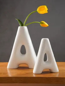 Modern white resin A-shaped vases displayed on a wooden surface with a yellow tulip