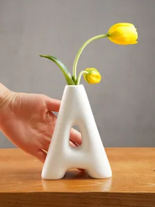 Close-up of minimalist A-shaped white resin flower vase on wooden table