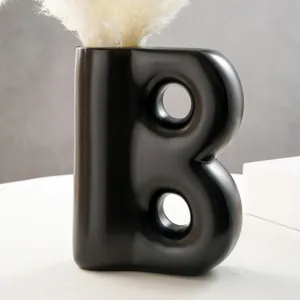 Dettaglio del moderno vaso in resina nero opaco a forma di B per decorazioni con fiori secchi