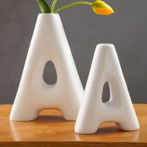 Modern white resin A-shaped vases displayed on a wooden table with a yellow tulip