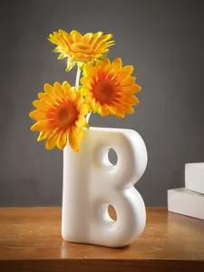Dettaglio di un vaso in resina bianca a forma di B con girasoli su un tavolo di legno.