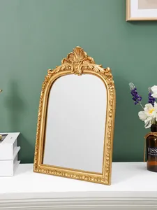 Vintage verzierter goldener Harzspiegel steht auf weißem Tisch vor grüner Wand