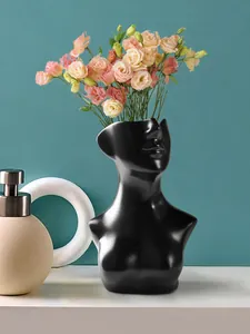 Detailansicht der modernen schwarzen Harzvase in Menschenform mit Blumen auf dem Tisch
