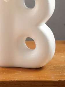 Dettaglio ravvicinato di un vaso in resina bianca a forma di B con texture opaca e curve