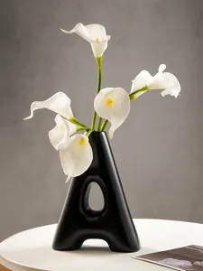 Detail of a minimalist black A-shaped resin vase with elegant white calla lilies.