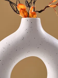 Detailopname van witte gespikkelde O-vormige keramische vaas met herfstblad