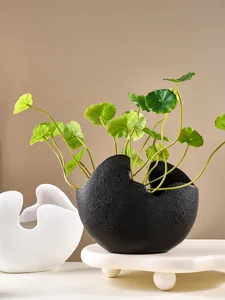 Detailweergave van een zwarte halfronde vaas van hars met kunstmatige groene planten