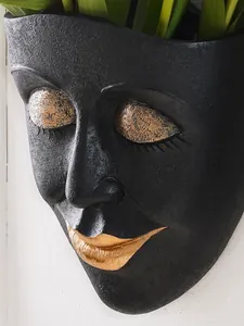 Close-up of a minimalist matte black resin face planter with gold lips and eyelids.