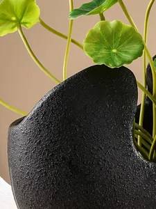 Macro-detail van een zwarte getextureerde harsvaas met groene kunstmatige plantenbladeren.