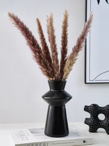 A detailed view of a black geometric lighthouse-shaped resin vase with pampas grass