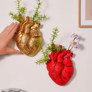 Vista detallada de jarrones de corazón anatómico rojos y dorados en pared blanca con plantas
