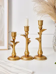 Macro view of three golden distressed palm tree candle holders on a white table.