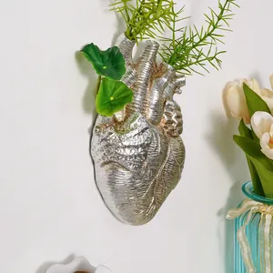 Detalle que muestra un jarrón de pared plateado con forma de corazón y plantas verdes
