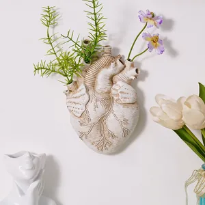 Primer plano de un jarrón de pared con forma de corazón nórdico y flores artificiales