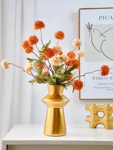 Modern golden lighthouse-shaped resin vase styled with artificial flowers on a white table.