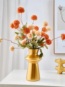 Close-up of golden lighthouse-shaped resin vase with orange artificial pom-pom flowers