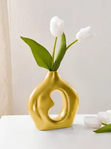 Nahaufnahme einer dekorativen goldfarbenen Keramikvase in Bohnenform mit Tulpen