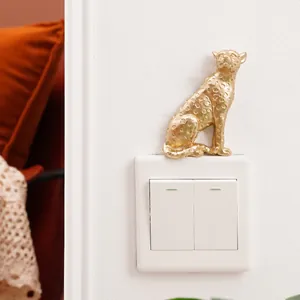 Close-up of a golden resin leopard figurine decorating a white wall light switch