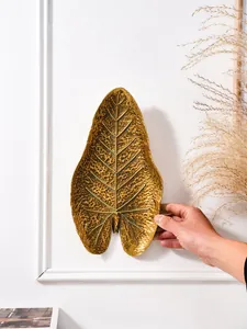Détail montrant la texture et la taille d'une décoration murale feuille tropicale en résine dorée.