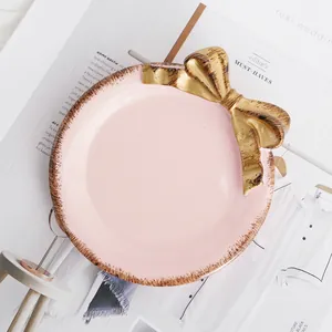 Vista detallada de una bandeja de cerámica rosa para joyas con un lazo dorado decorativo