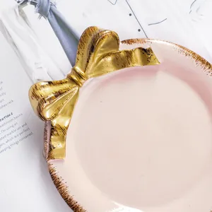 Detalle macro de una elegante bandeja de cerámica rosa para joyas con un lazo dorado