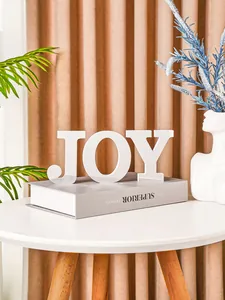 Detail view of mirror finish JOY letter ornament on a wooden table in a cozy room.