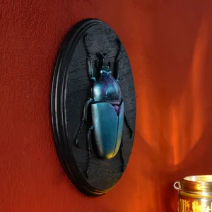 Detail view of a 3D metallic blue beetle resin wall plaque on a red textured wall