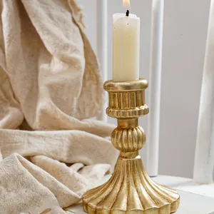 Primer plano de un candelabro vintage de resina con forma de columna romana dorada y una vela.