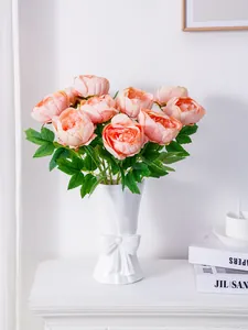 Elegantes peonías artificiales de tela rosa en un jarrón blanco con lazo para decorar