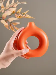 Detail van een minimalistische oranje O-vormige keramische vaas vastgehouden in hand