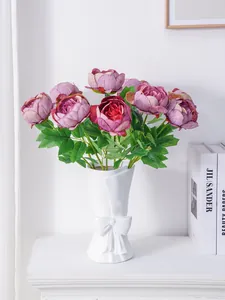 Elegantes peonías púrpuras artificiales en un jarrón blanco con lazo para decoración