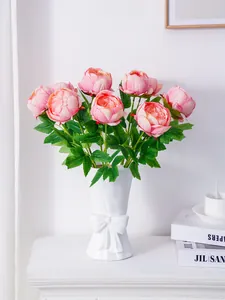 Vista detallada de peonías artificiales rosas en un jarrón blanco decorado con un lazo
