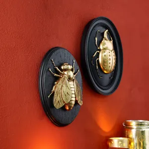 Close-up of vintage gold beetle and bee resin wall relief decorations on red wall