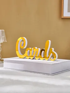 Close-up of golden mirrored 'Cards' acrylic sign on a white book for wedding decor