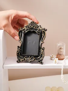 Hand holding vintage black and gold embossed frame on a decorative shelf display